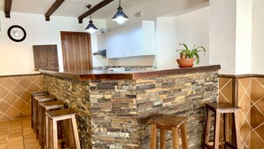 Une cuisine dotée d’un îlot central en pierre, de tabourets en bois, de luminaires suspendus et d’une horloge au mur.