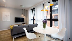 Una sala moderna con un sofá gris, sillas blancas, una mesa redonda blanca y un televisor montado en la pared.