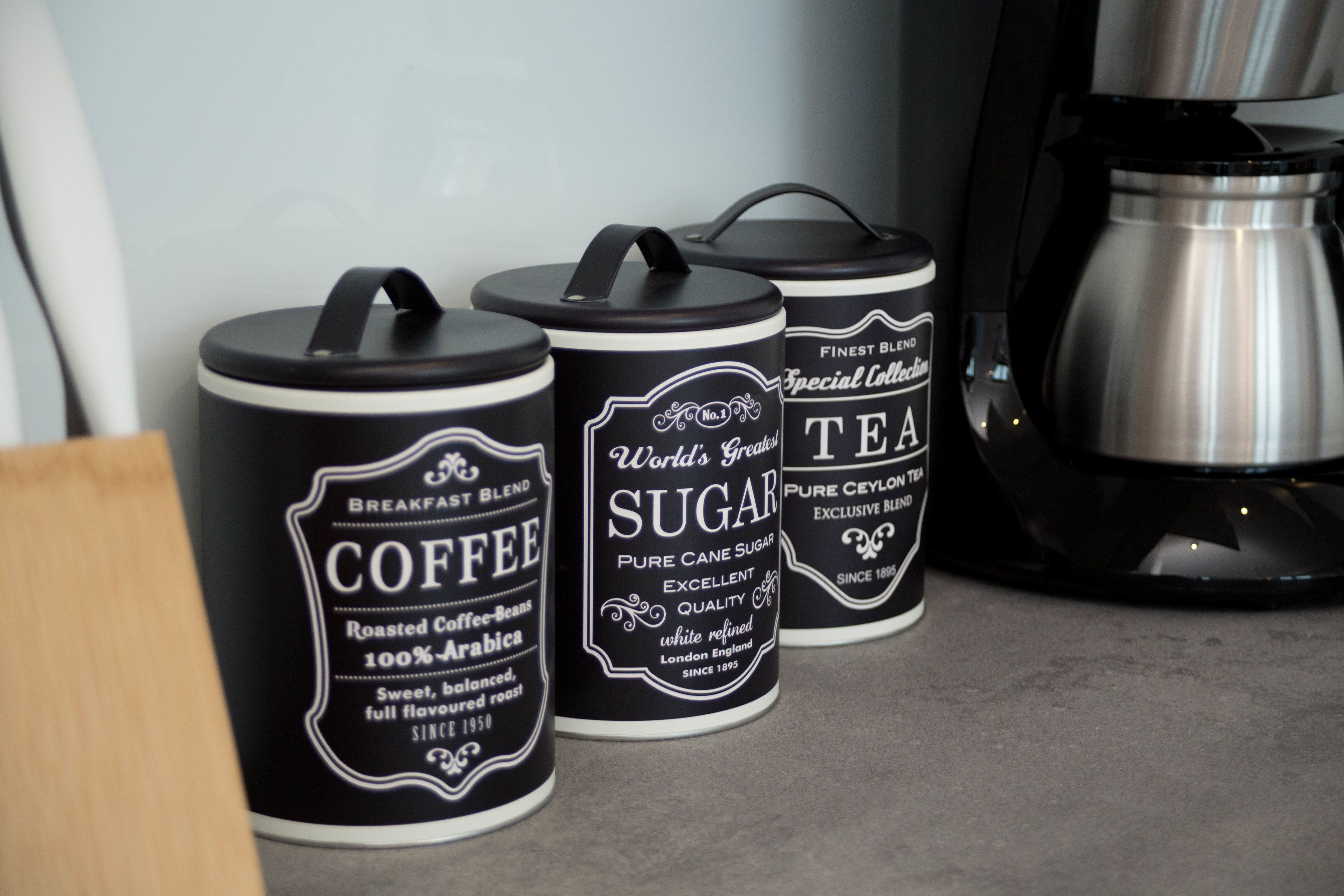 Drie zwarte containers met witte labels op een aanrecht.