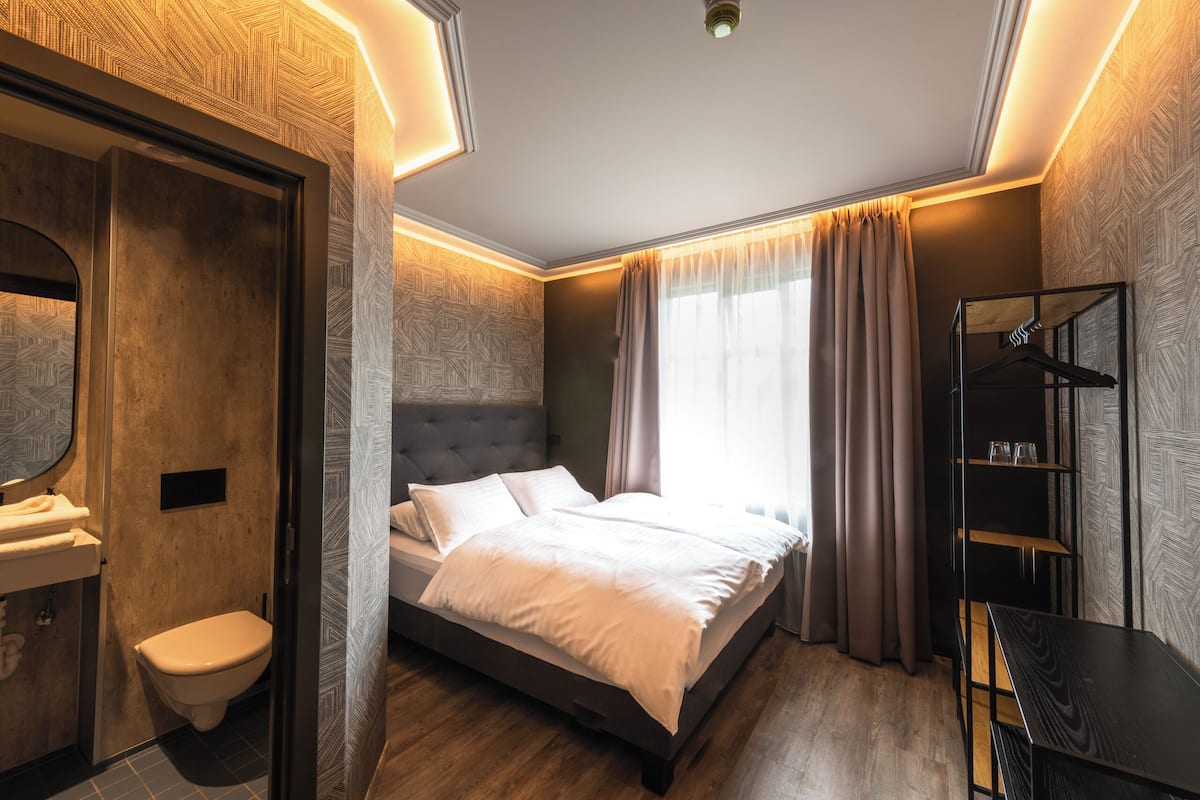 Un dormitorio moderno con cama, mesita de noche, armario y baño con inodoro y lavabo.