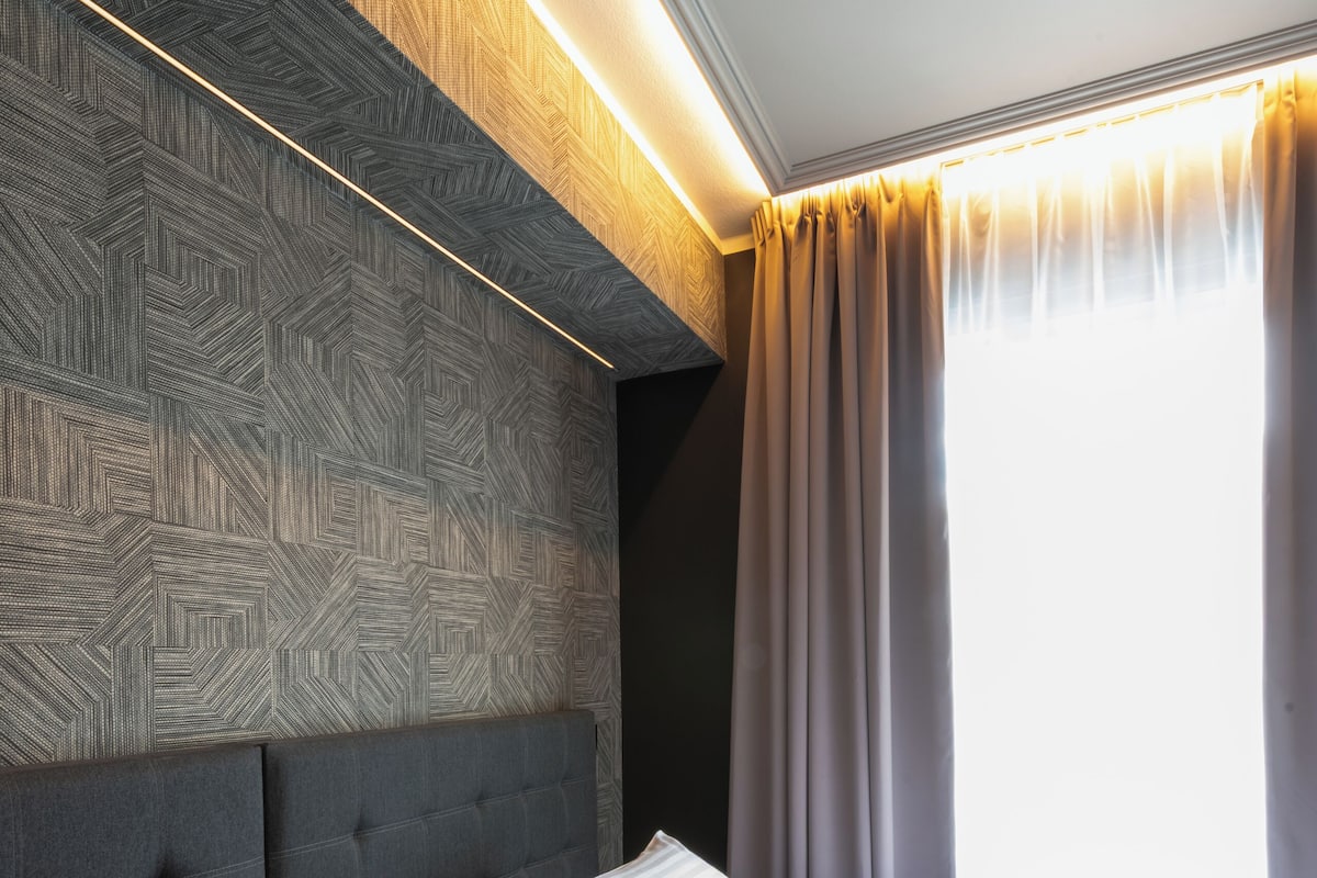 A hotel room with a modern design, featuring a large bed with white linens, a tufted headboard, and a geometric-patterned wall.