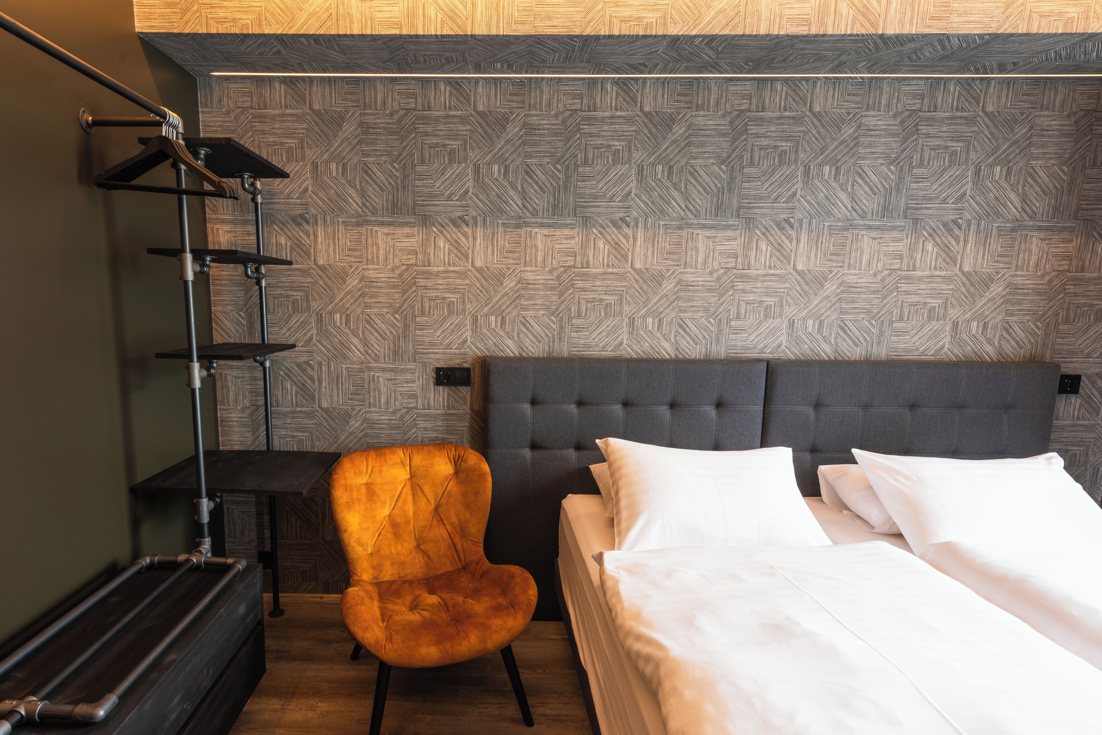 Una habitación de hotel con una cama, una silla, un escritorio y una pared con un diseño geométrico.