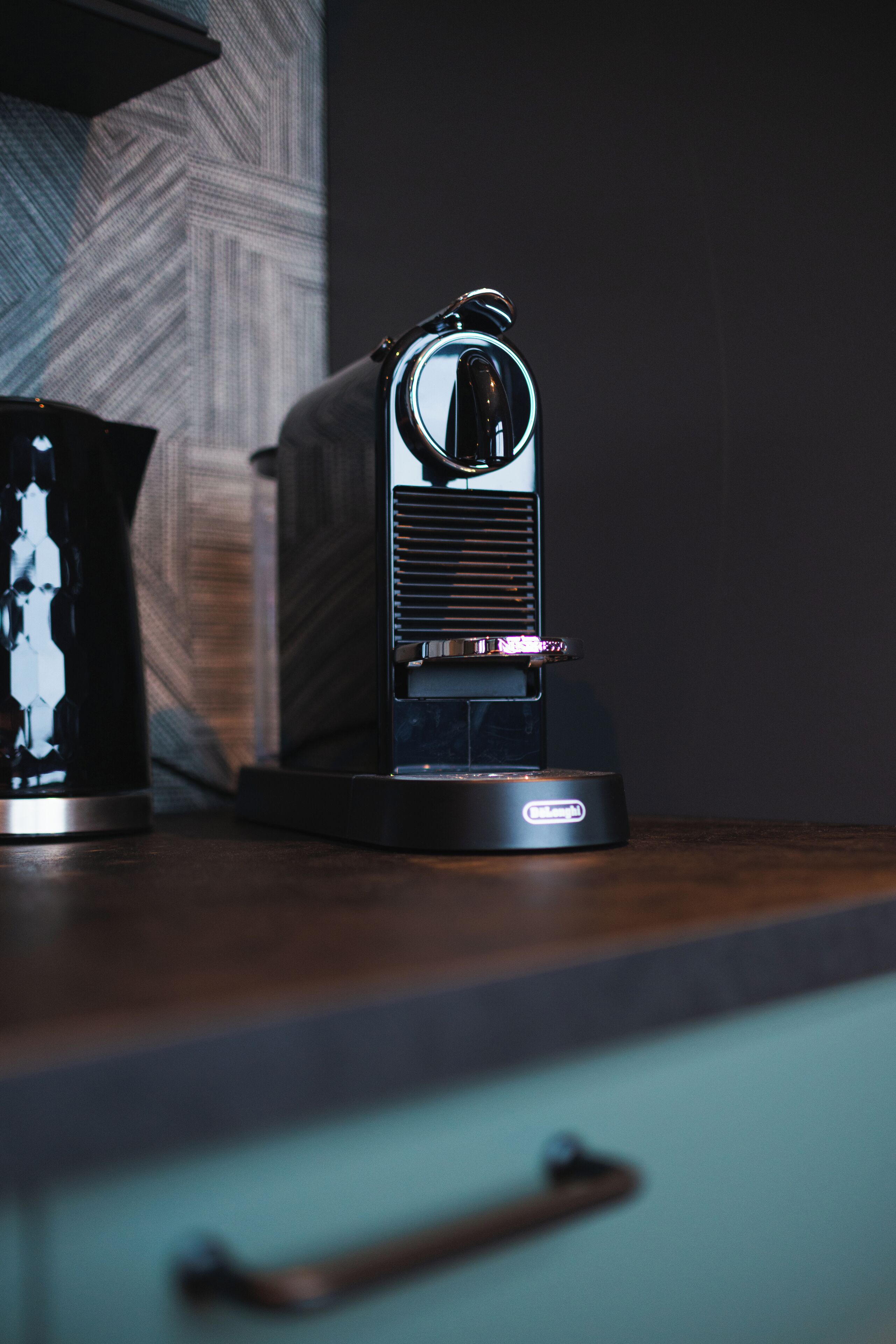 A coffee machine on a wooden countertop with a textured wall in the background.