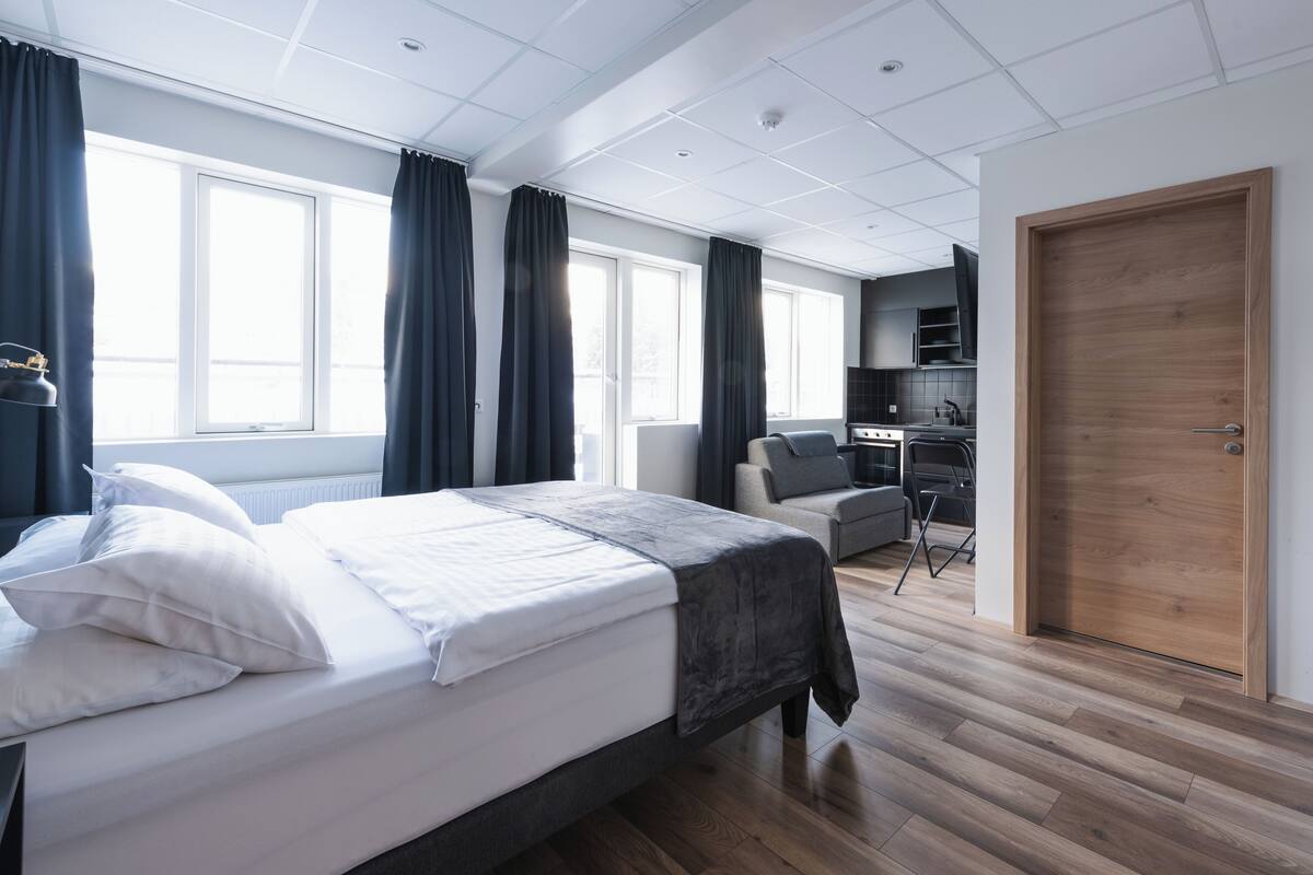 A modern hotel room with a large bed, a desk, and a kitchenette.