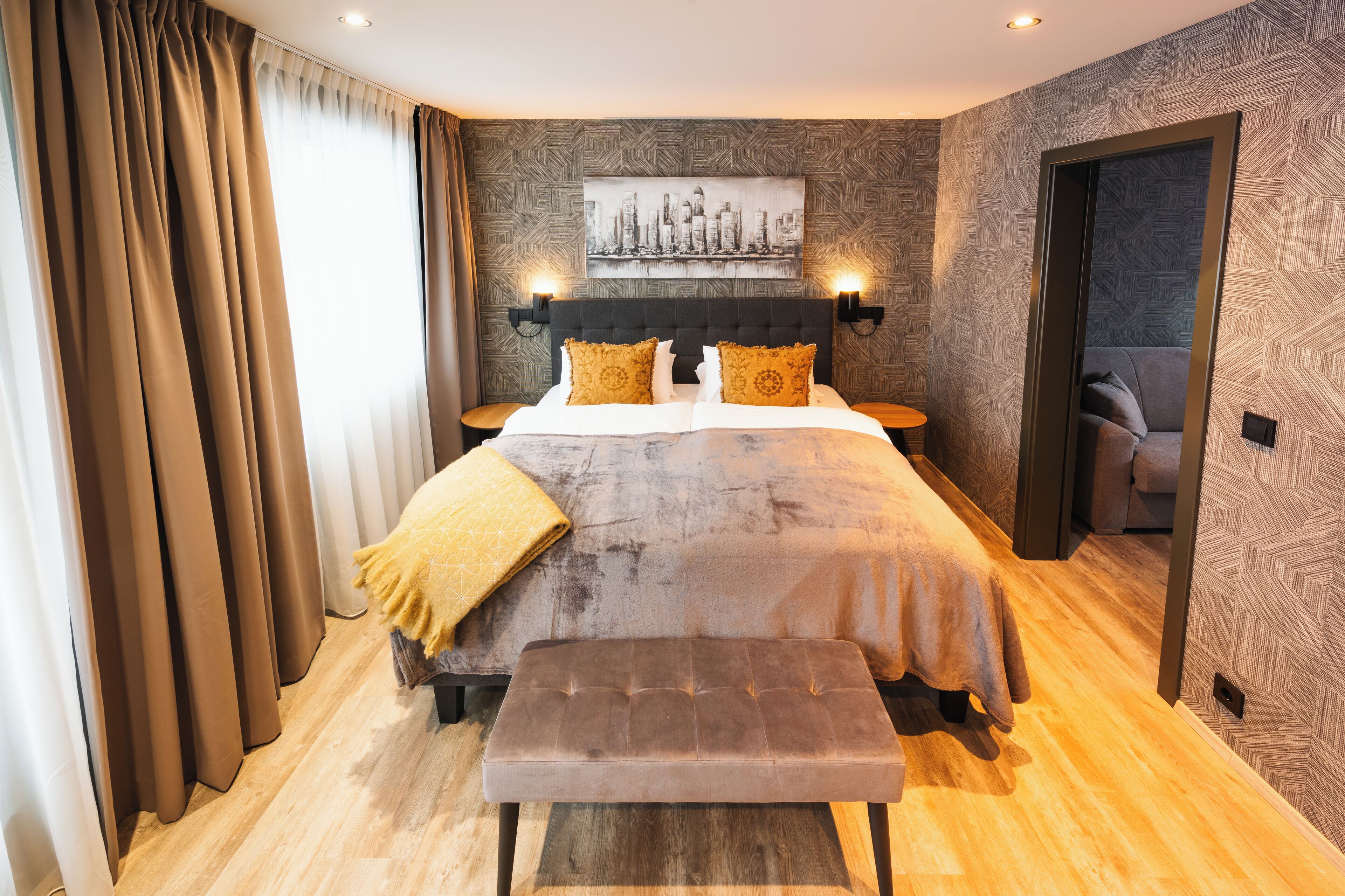 A modern hotel room with a large bed, a bench, and a cityscape artwork on the wall.