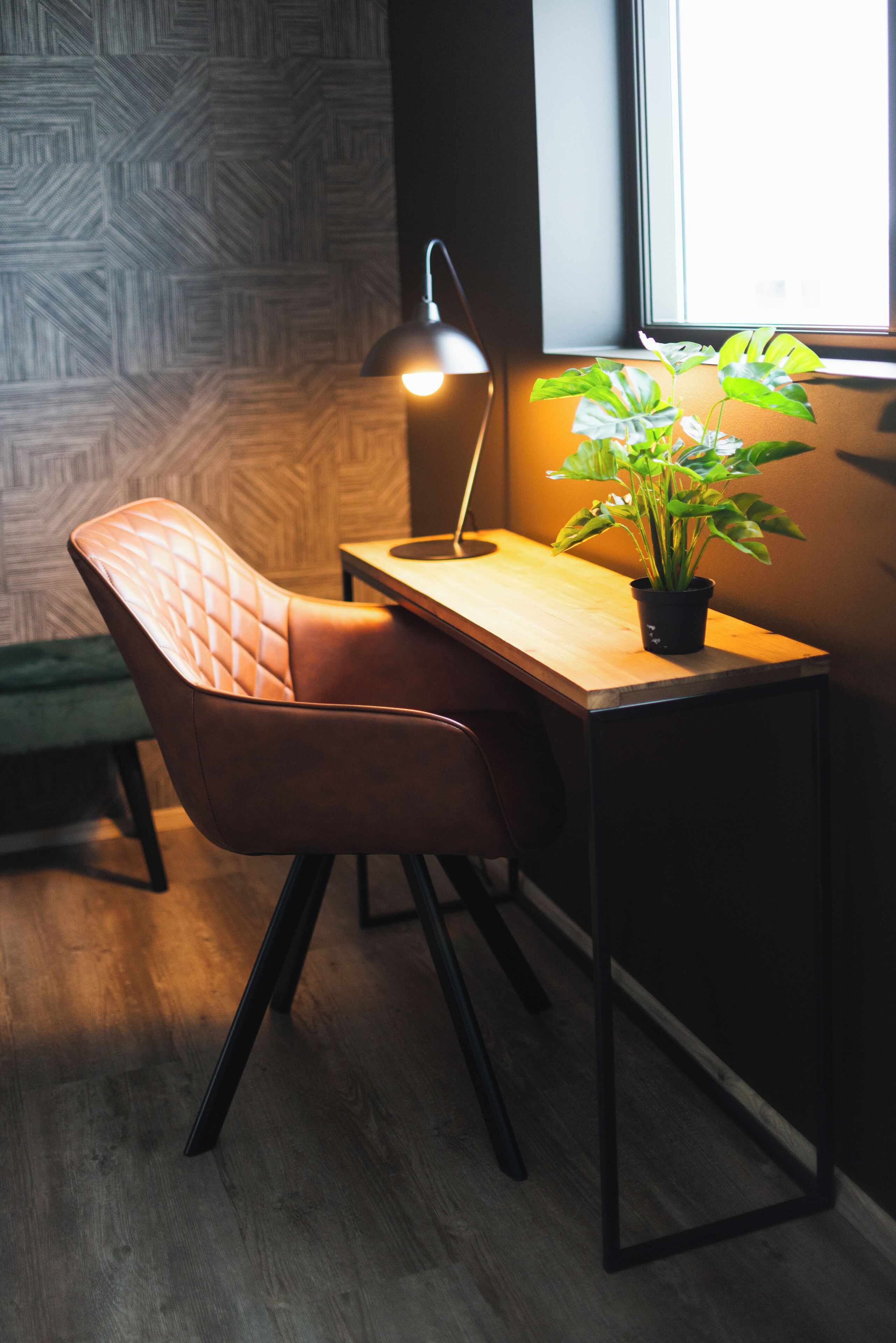 Une pièce moderne avec un bureau en bois, une chaise rembourrée, une lampe sur pied et une plante en pot.