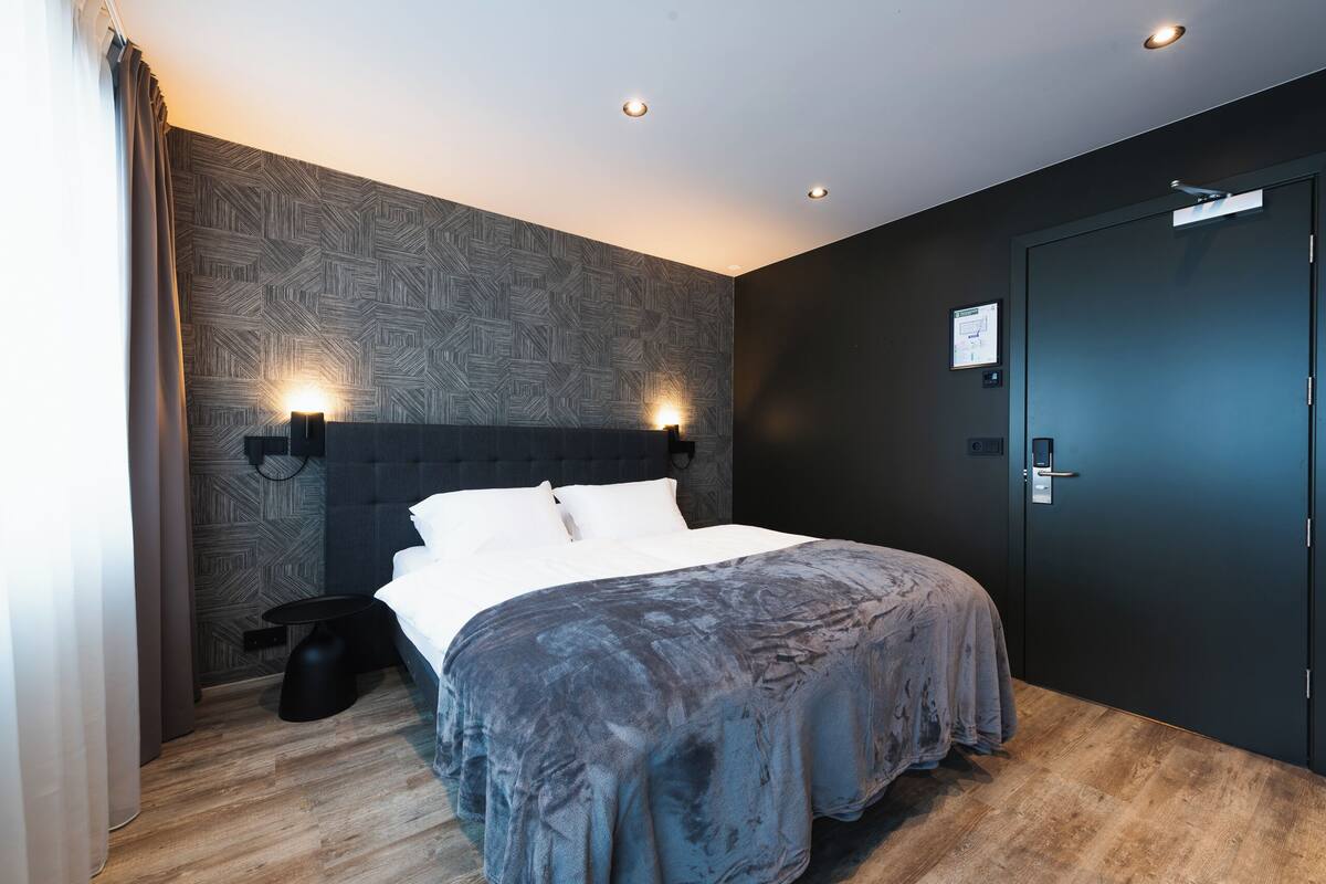 Una habitación de hotel moderna con una cama grande, un cabecero oscuro y un papel tapiz estampado.