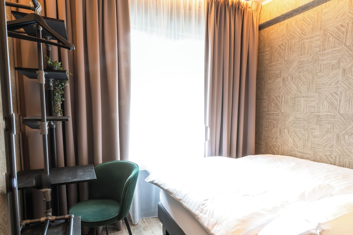 A modern hotel room with a bed, desk, chair, and a view of the outdoors.