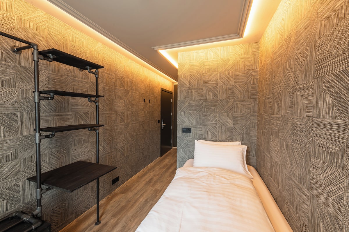 A hotel room with a bed, a shelf unit, and patterned wallpaper.