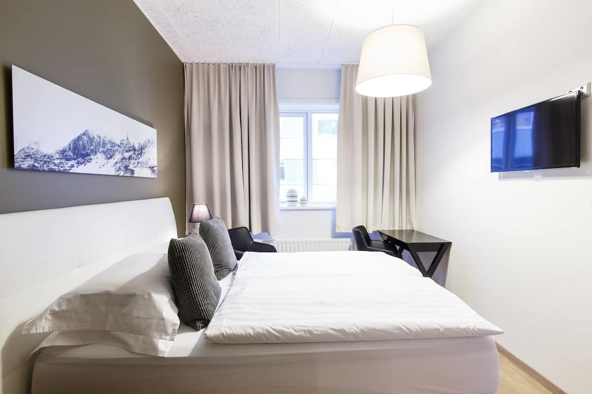 A hotel room with a bed, a desk, a chair, a TV, and a window with curtains.