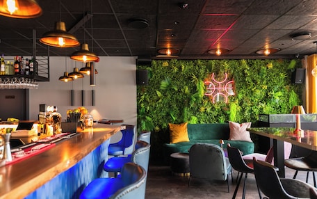 A bar area with a green wall, bar stools, and a neon sign.