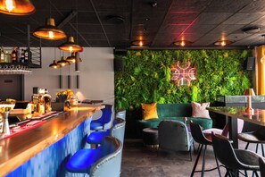 Zona de bar con pared verde, taburetes y un letrero de neón.