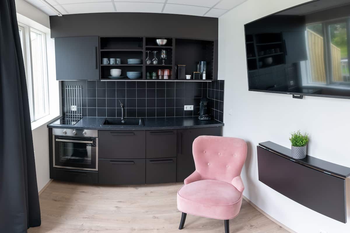 A modern kitchen with black cabinetry, a pink chair, and a flat-screen TV mounted on the wall.