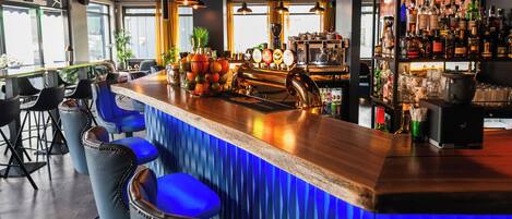 A bar area with a wooden counter, blue bar stools, and hanging pendant lights.