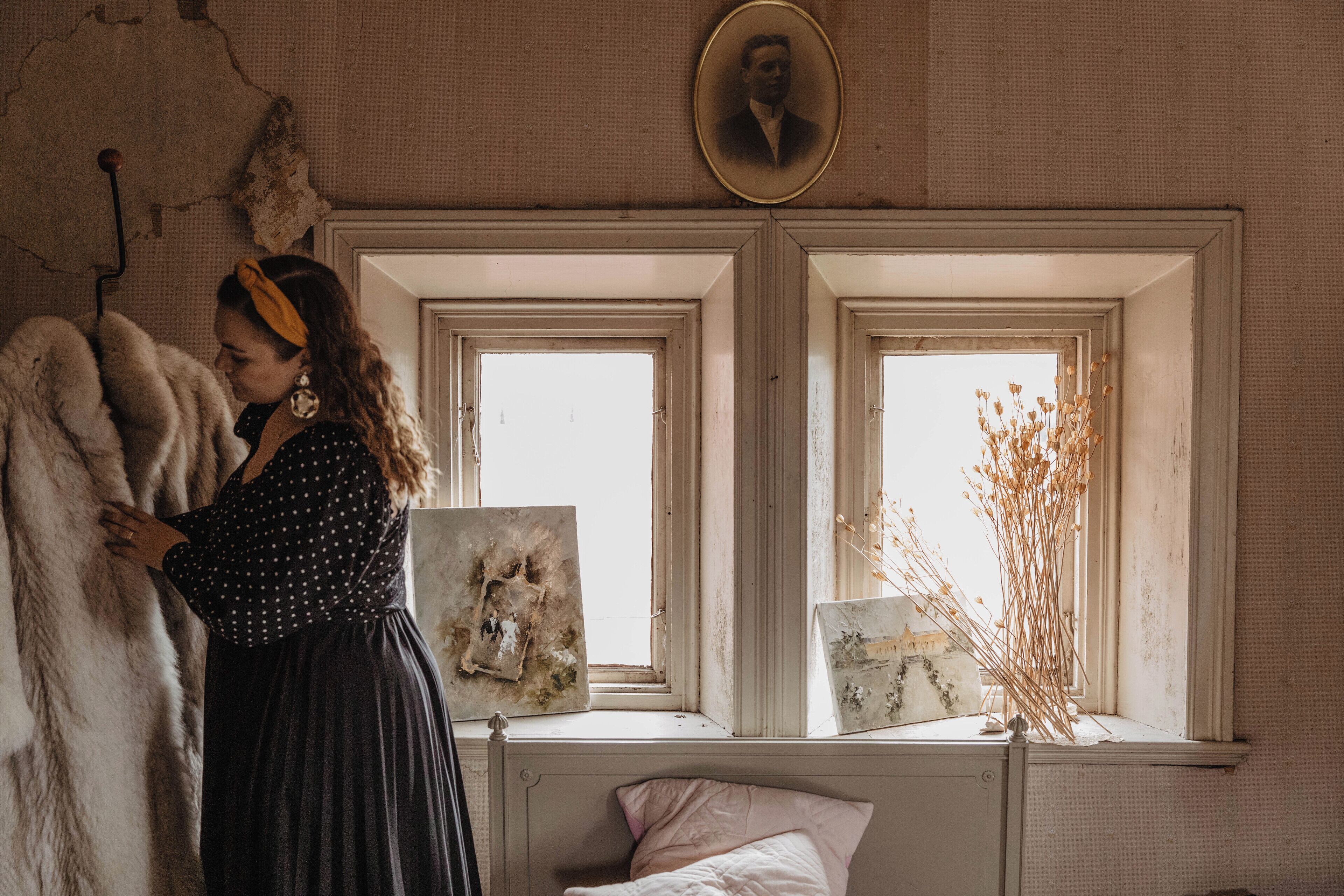 Una habitación con una cama, dos ventanas y una pared con un retrato y un marco de fotos.
