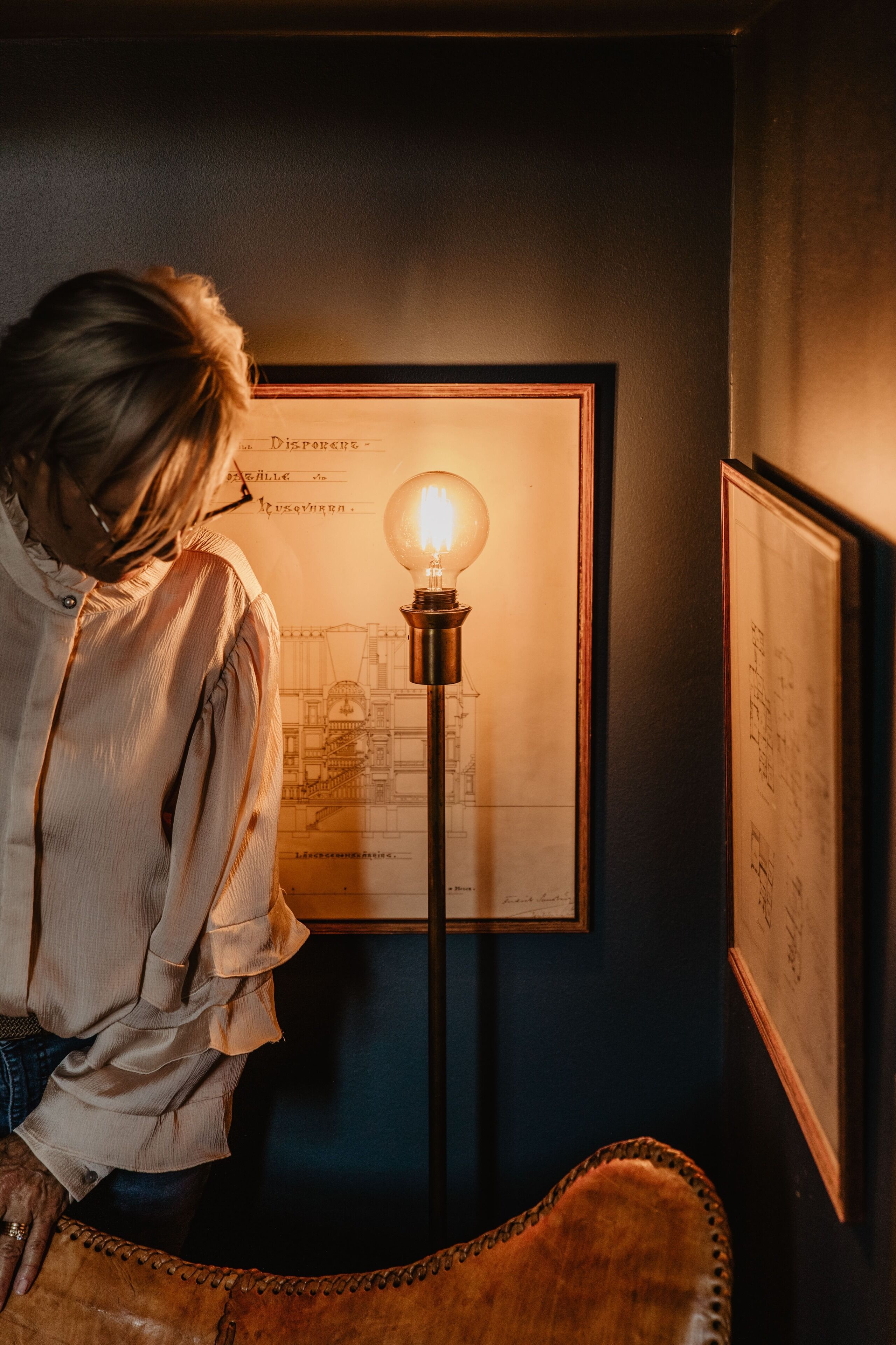 A person standing in front of a framed architectural drawing with a light bulb on a stand.
