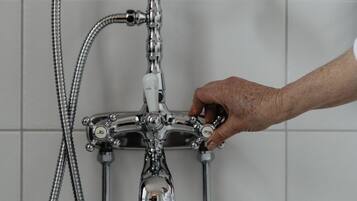A bathroom with a vintage-style shower system, including a handheld showerhead and a flexible hose.