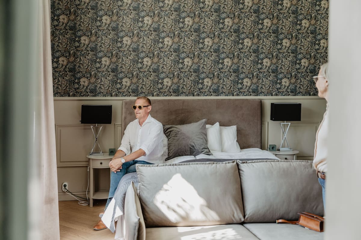 Une chambre à coucher avec un grand lit, deux tables de chevet avec des lampes, une tête de lit à motifs floraux et un mur uni.
