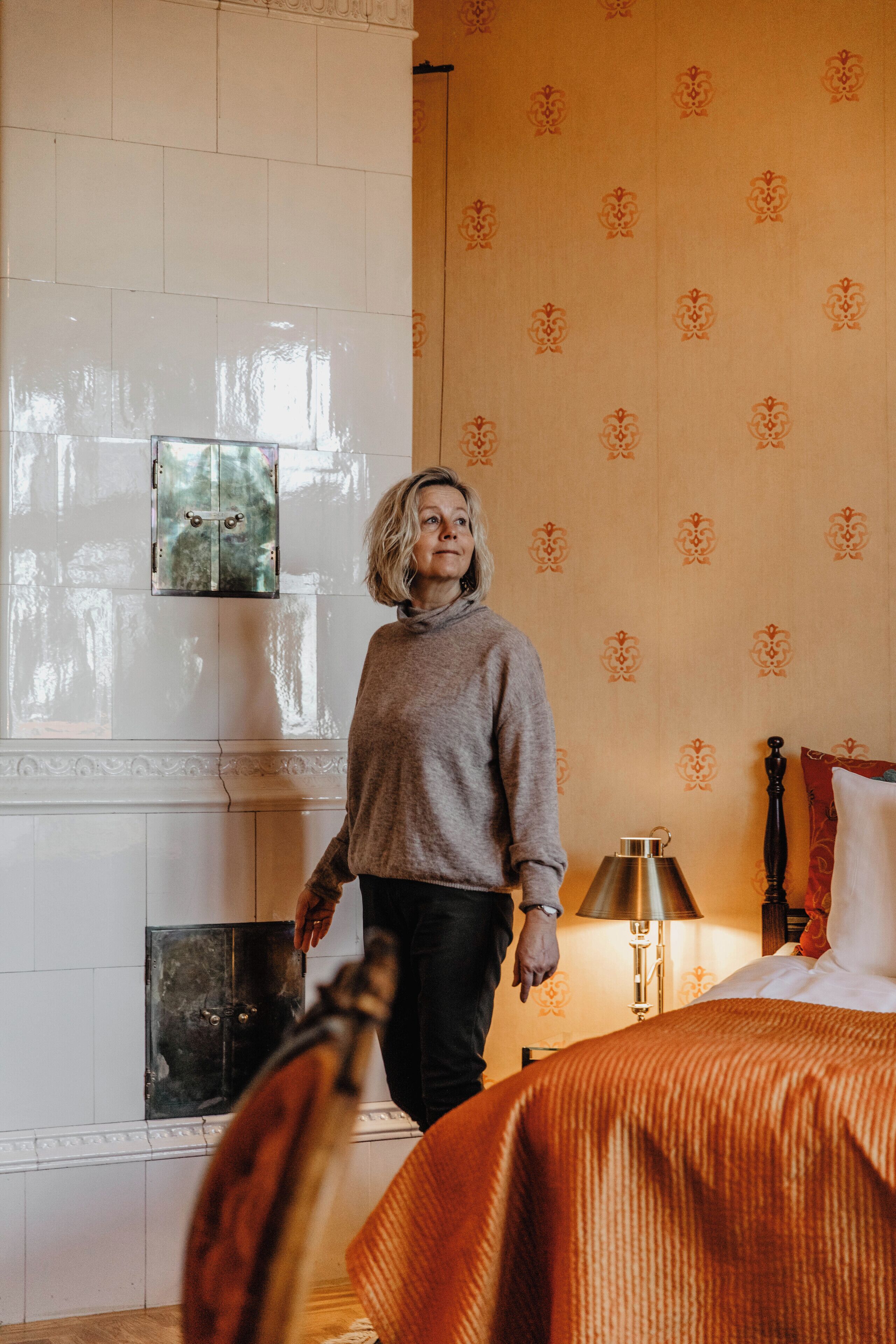 Ein Zimmer mit Kamin, einem Bett mit orangefarbener Bettdecke und einer Wand mit Muster.