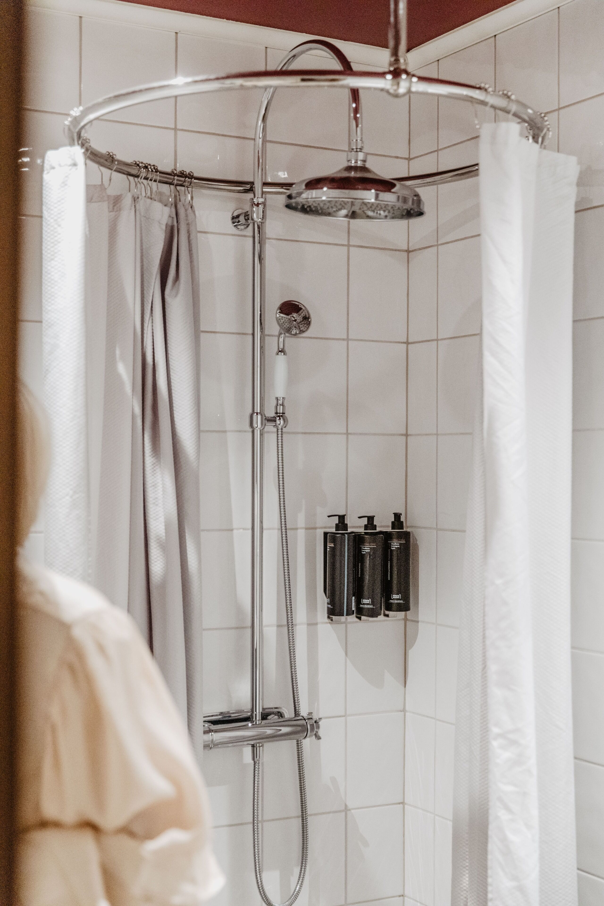 Une douche avec une porte en verre, un pommeau de douche à main et deux bouteilles de shampoing et d’après-shampoing fixées au mur.