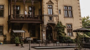 Un edificio histórico con balcón, mesas al aire libre y un letrero que dice