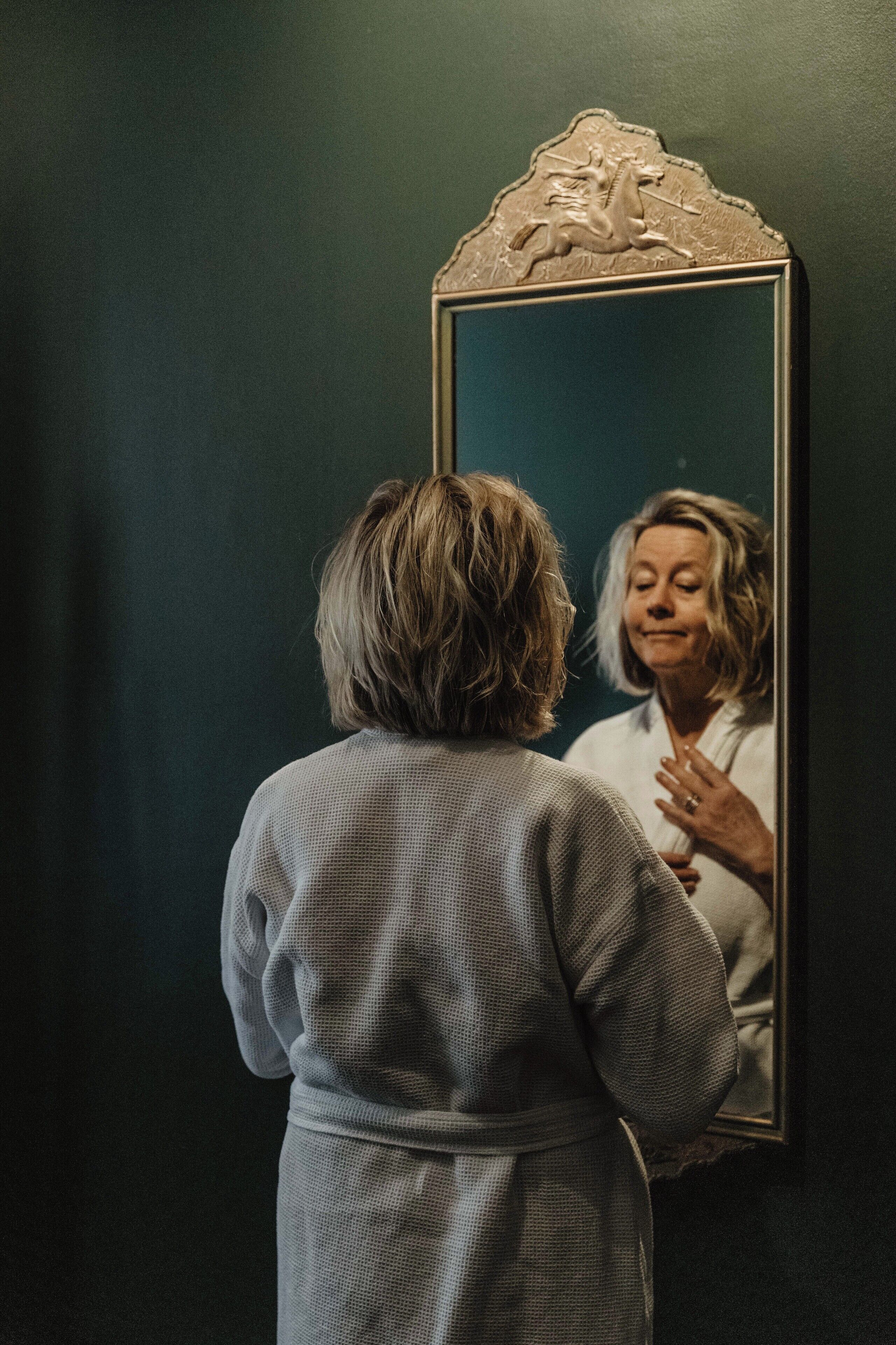 A person in a robe standing in front of a mirror with an ornate frame.