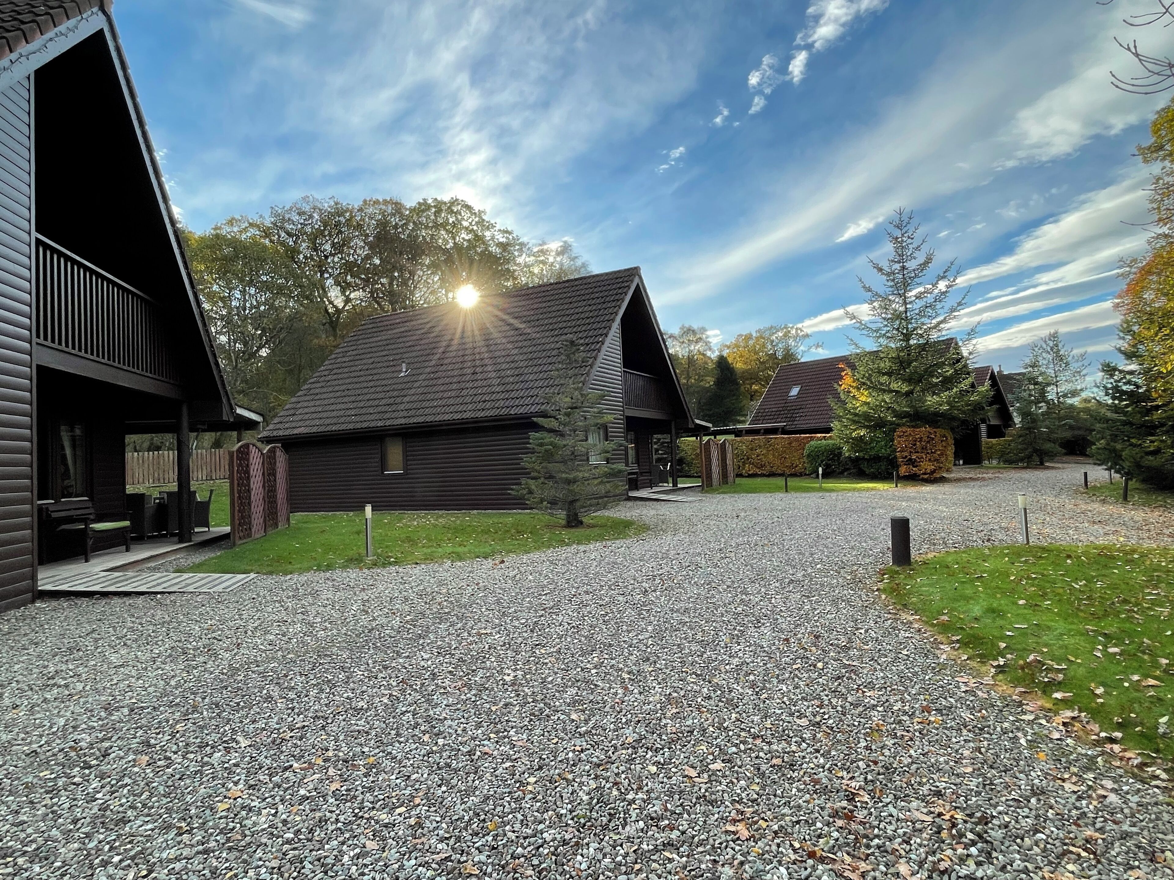 A gravel driveway leading to a row of log cabins with a clear sky above.