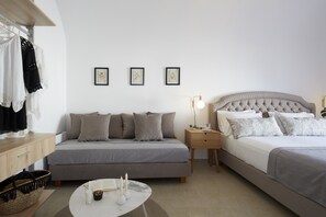 Un dormitorio moderno con un sofá gris, una cama con ropa de cama gris, una mesita de noche con una lámpara y una pequeña mesita auxiliar con una taza y un platillo.