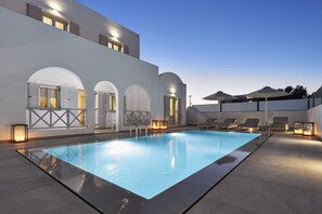 A modern pool area with a rectangular pool, lounge chairs, and a building with arched doorways and lighting. - Tramonto Private Villa (Santorini)