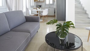 Una sala de estar moderna con un sofá gris, una mesa de centro redonda de vidrio con una planta, y una escalera que conduce a una zona de cocina.