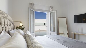 Un dormitorio con cama, mesita de noche, espejo y vistas al cielo a través de una ventana abierta.