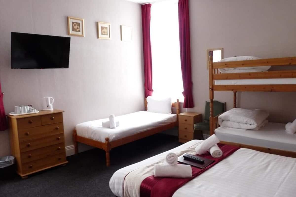 Habitación de hotel con literas, cama individual, cómoda de madera, televisor de pantalla plana y ventana con cortinas.