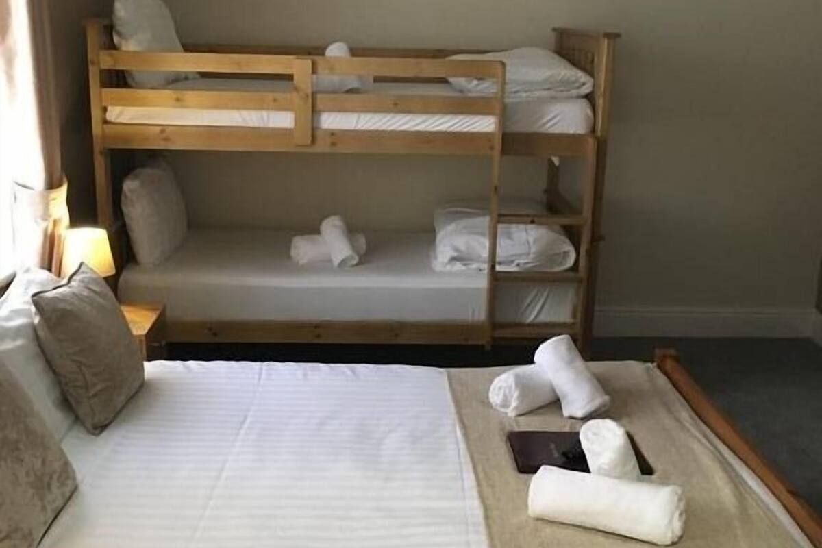 Cama litera con ropa blanca y toallas, una cama individual con ropa blanca y una lámpara sobre una mesita de noche.