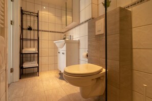 A bathroom with a toilet, a sink, and a shelf with towels. - Bjarmó Guesthouse (Akureyri)