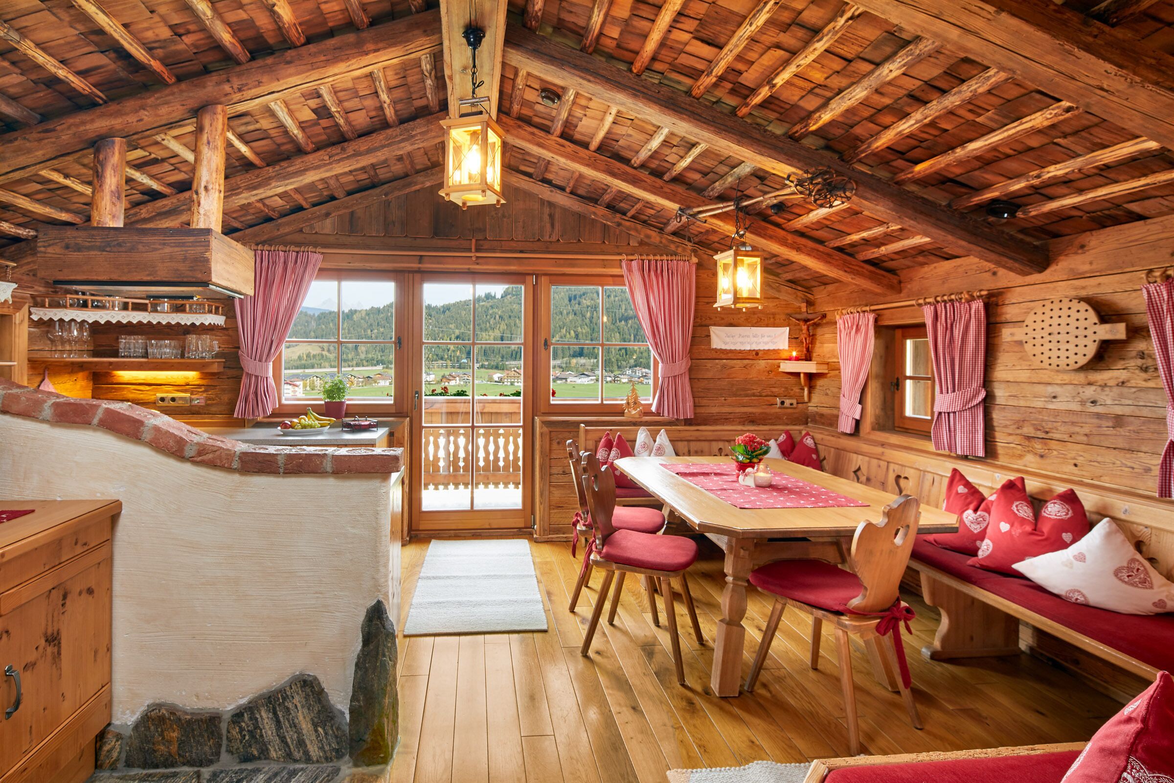 A wooden cabin with a dining area, a kitchen with a bar, and large windows offering a view of the outdoors.