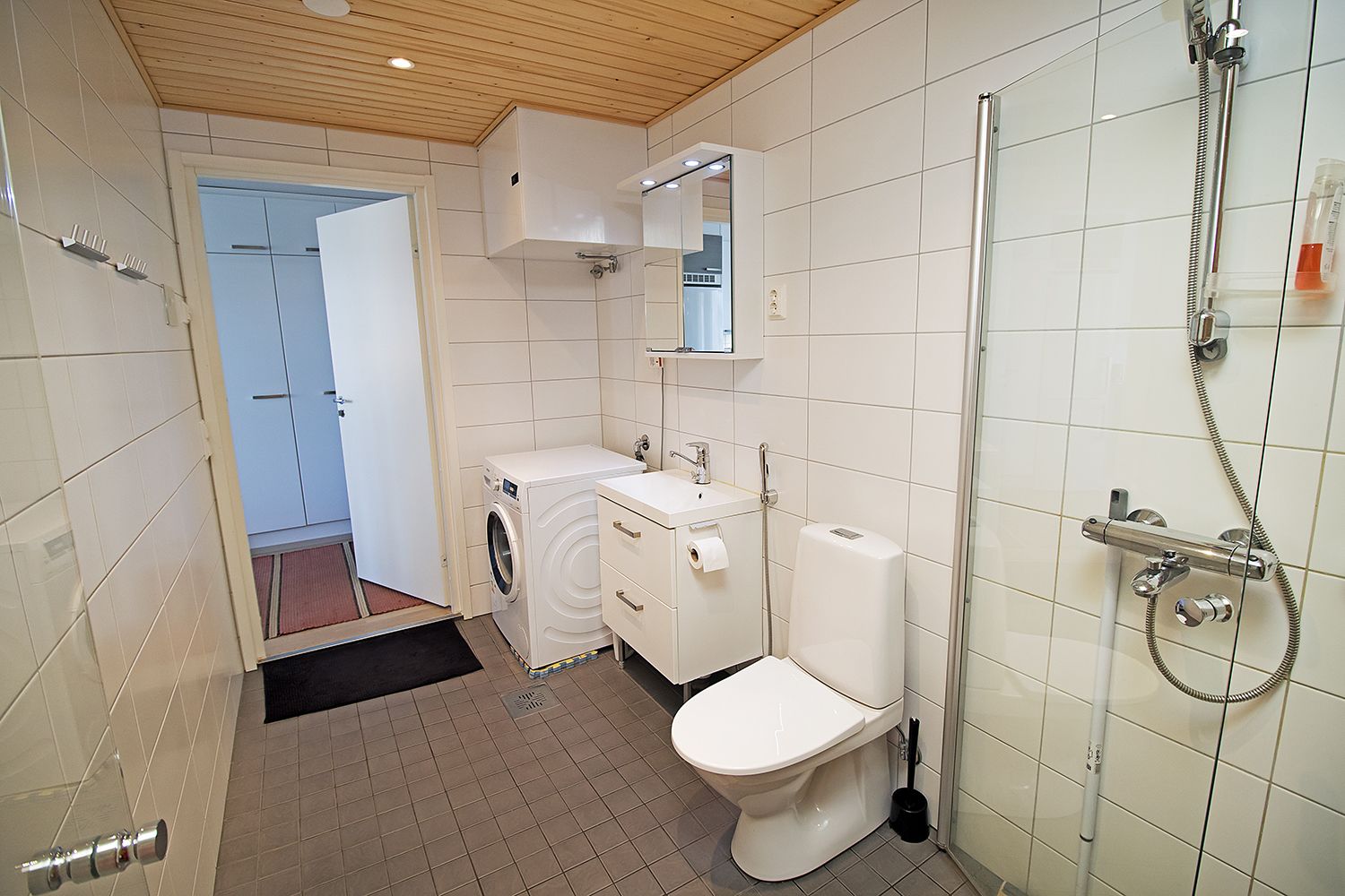 A modern bathroom with a washing machine, a toilet, and a shower.