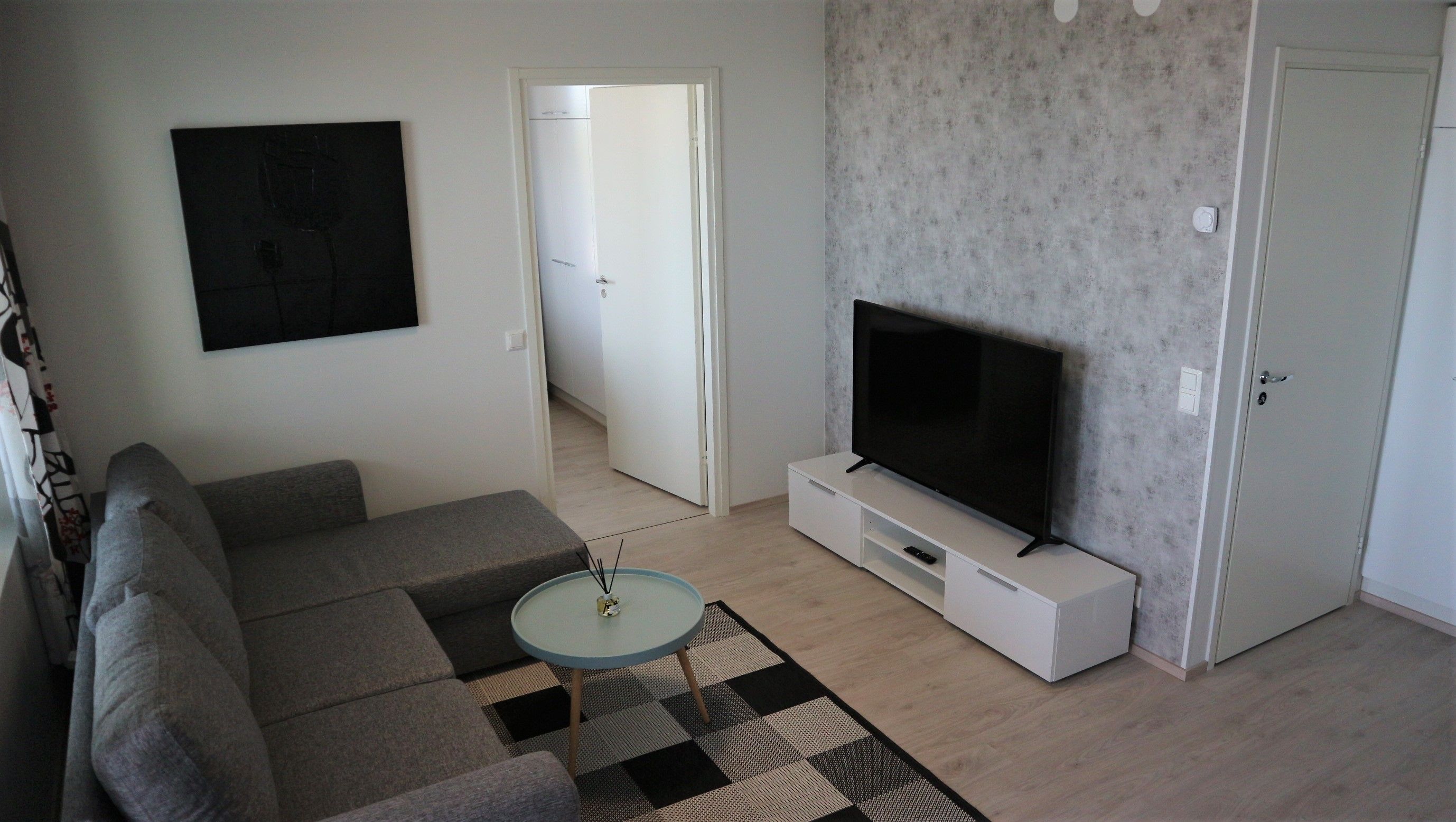 A living room with a sofa, a coffee table, a TV on a stand, and a door leading to another room.
