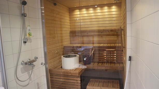 Una sauna con interior de madera, puerta de vidrio y zona de ducha con cabezal de ducha manual.