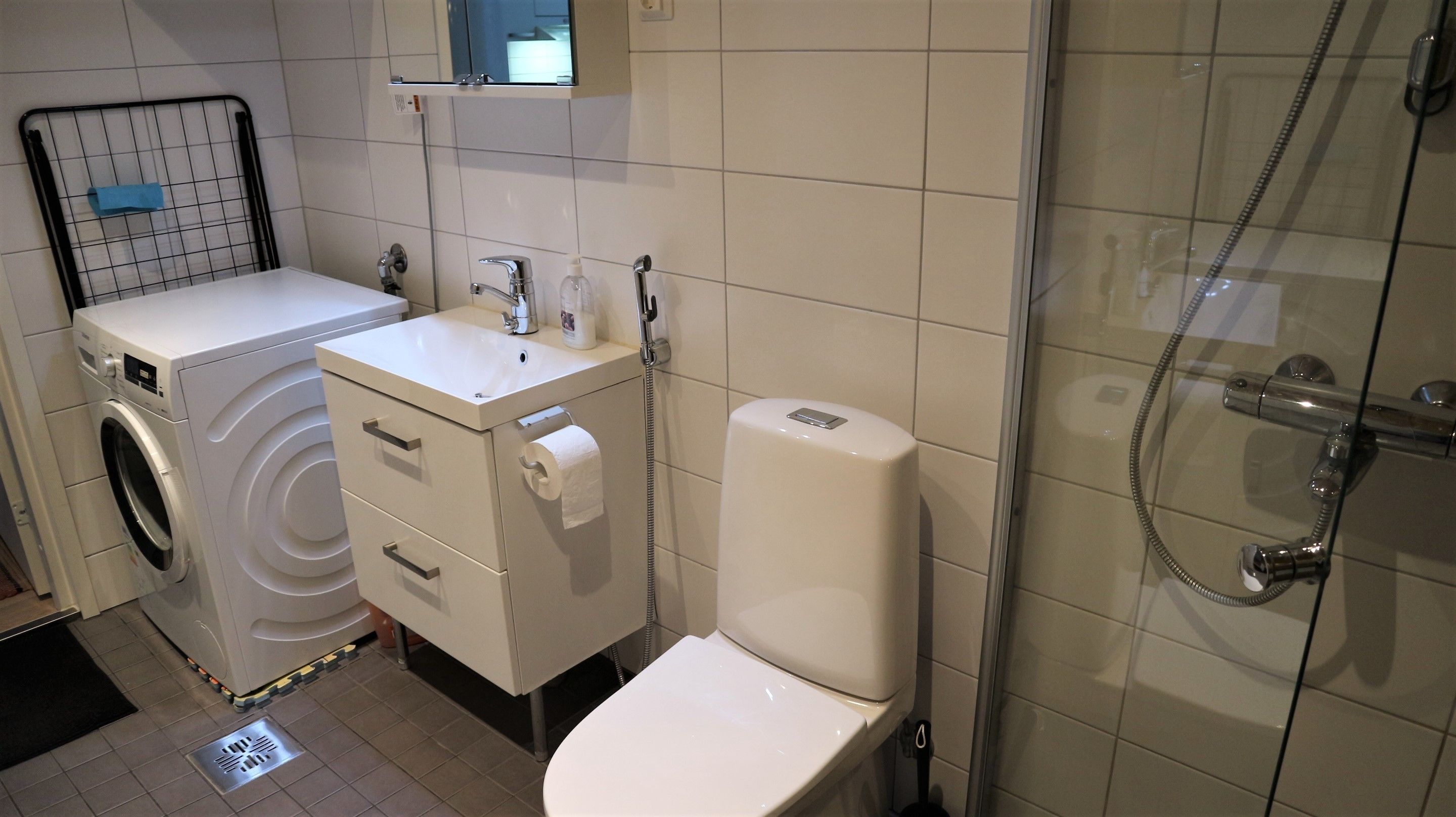 A compact bathroom with a washing machine, a sink, a toilet, and a shower.