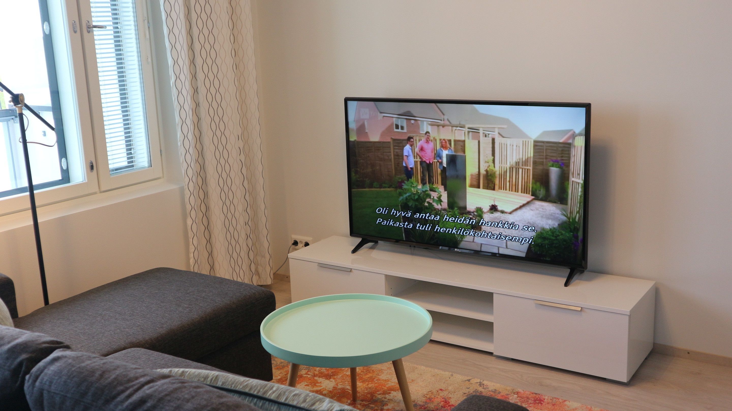 A modern living room with a flat-screen TV on a white stand, a grey sofa, and a small round table.