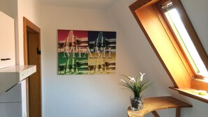 A hallway with a wooden staircase, a wall-mounted picture of Miami's skyline, and a small plant on a wooden shelf.