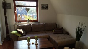 A cozy living room with a sectional sofa, a wooden coffee table, and a window with a view of a building outside.