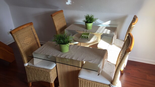 A dining area with a glass table, wicker chairs, and a potted plant.