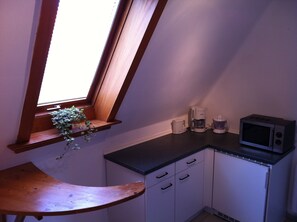 A small kitchenette with a window, a microwave, a coffee maker, and a wooden bench. - Zimmervermietung Arp 17 (Itzehoe)