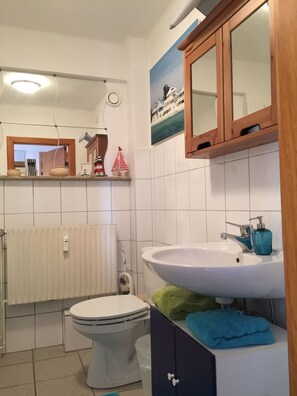 A bathroom with a white sink, a mirror, a toilet, and a towel rack. - Zimmervermietung Arp 17 (Itzehoe)