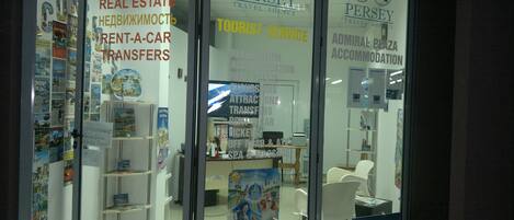A travel agency with glass doors, offering services like excursions, real estate, and car rentals. Inside, there are chairs and a desk with a computer.