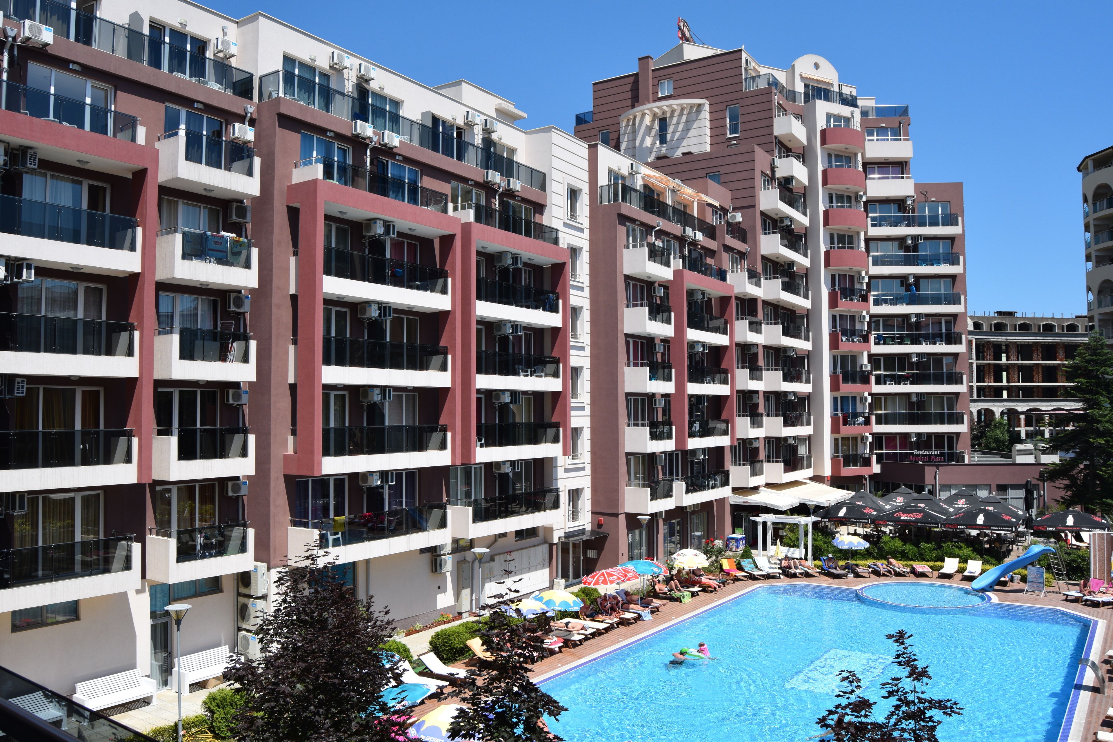 Ein mehrstöckiges Hotel mit Balkonen, einem Schwimmbad und Außenbereichen zum Sitzen.