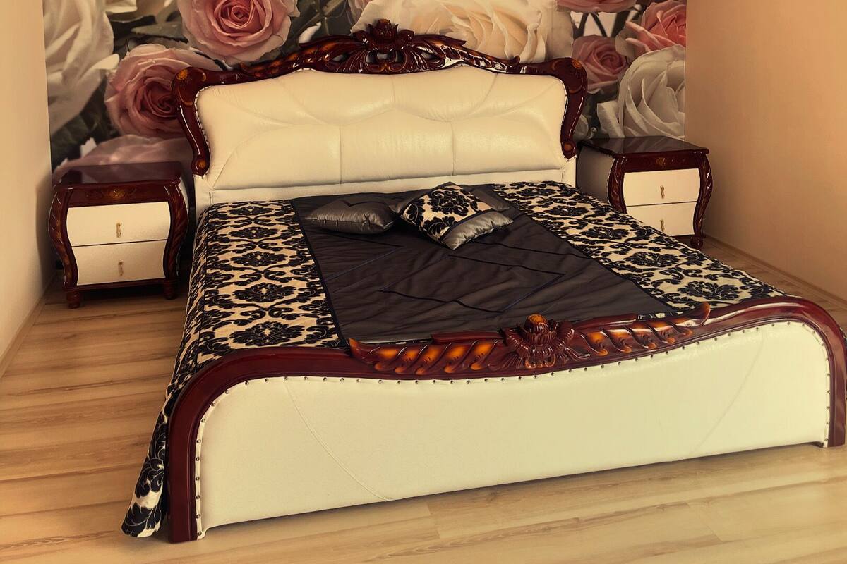 Een slaapkamer met een groot bed, een kroonluchter en een rozenmotief op de muur.