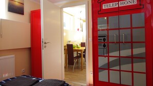 Una habitación con una cama, un armario rojo con teléfono y una puerta que da a un comedor.