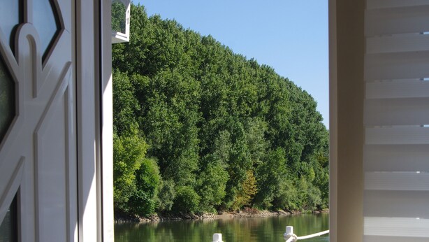Vista desde una habitación con puerta a un balcón con vista a un río y zona boscosa.
